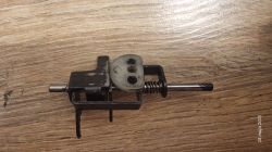 Część mechanizmu młotowiertarki z widoczną sprężyną i metalowymi elementami na drewnianym blacie.