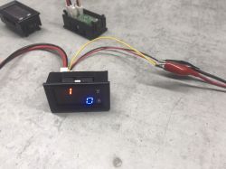 Digital voltage and current meter with display showing incorrect reading of 52A with thick wires disconnected.