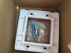 White mounting part in a cardboard box; plastic bag with two blue screws and a piece of metal mesh