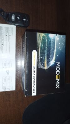 Pilot samochodowy z trzema przyciskami oraz pudełko sterownika centralnego zamka MODEMIX na stole.