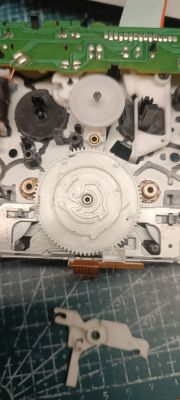 Wnętrze mechanizmu magnetofonu z dużą białą zębatką i elementami na stole warsztatowym