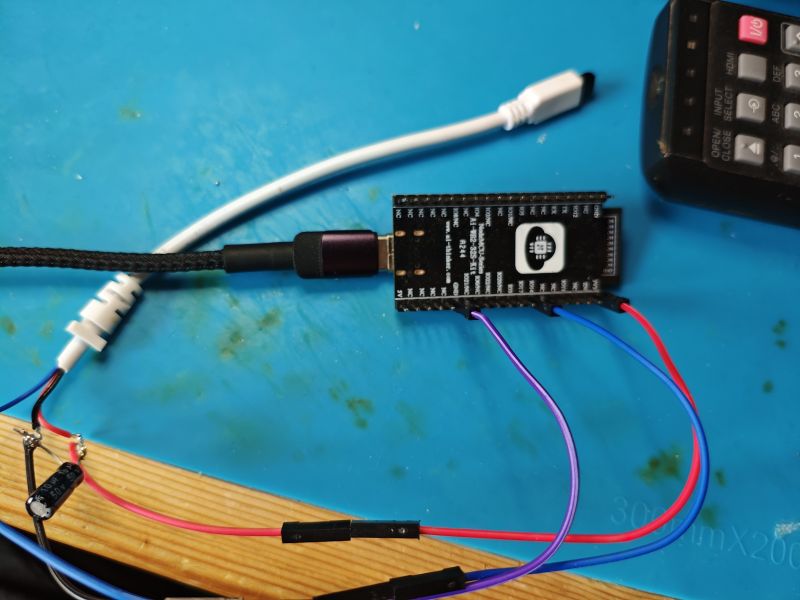 ESP32 development board with connected wires, capacitors, and USB-C cable on a blue service mat.
