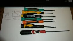 Zestaw kolorowych wkrętaków leżących na kartce papieru z rysunkiem technicznym w tle.