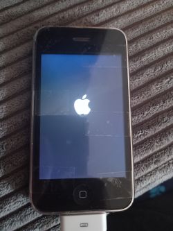 Telefon z logo Apple i ikonką ładowania zawieszony na ekranie startowym.