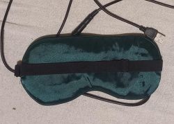 Zielona opaska na oczy z przewodem i wtykiem USB, leży na jasnej tkaninie