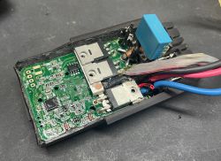 Płytka elektroniki w czarnej obudowie z przewodami i niebieskim kondensatorem, zbliżenie