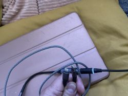 Zdjęcie kabla USB-C i Lightning trzymanego nad brązowym etui na laptop na żółtej poduszce.