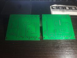 Two green PCB boards shown from the back with traces and solder points, lying on a dark desk.