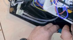 Wnętrze ekspresu Krups EA81 z widocznymi przewodami i rękami osoby naprawiającej przezroczysty wężyk.