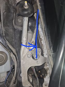 Część mechanizmu wycieraczek samochodowych z niebieską linią wskazującą element.