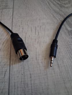 Kabel z jednej strony zakończony wtyczką DIN, z drugiej wtykiem jack 3.5 mm, oba na jasnej powierzchni.
