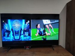 Telewizor wyświetlający dwa programy telewizyjne jednocześnie: quiz telewizyjny po lewej i transmisję sportową po prawej.