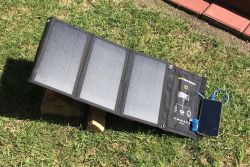 Foldable solar panel on grass, propped on wood blocks, with a connected device