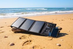 Foldable solar panel and smartphone on a beach, positioned on a piece of driftwood