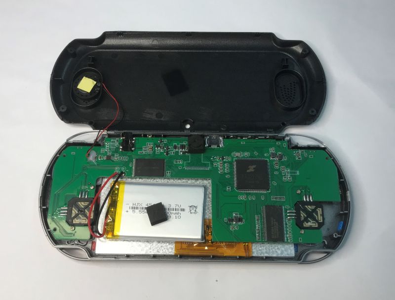Inside a handheld console: green PCB, Li‑ion battery, and speaker in an opened black case