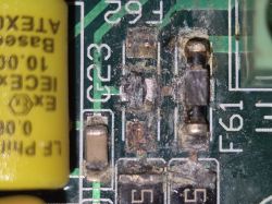 Uszkodzone elementy elektroniczne na zielonej płytce PCB z widocznymi śladami korozji