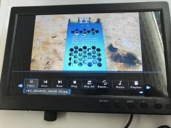 Small monitor with media player UI, showing a photo of a metal power supply in a blue perforated case.