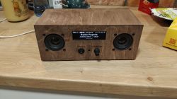 Wooden radio with two speakers and a display showing “Radio Pogoda” on a kitchen countertop