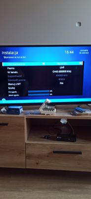Telewizor wyświetlający menu instalacji z informacją o zerowym sygnale, ustawiony na drewnianej szafce z elementami anteny.
