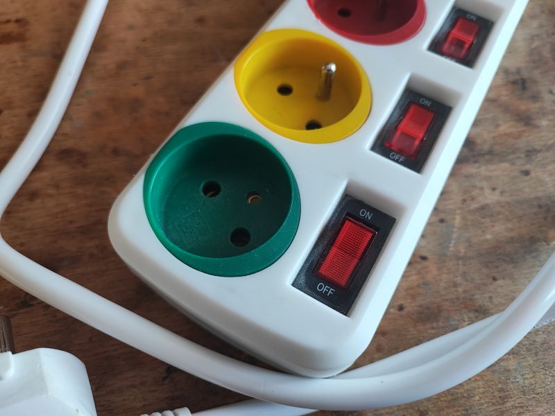 Kolorowa listwa zasilająca z osobnymi włącznikami i uszkodzonym uziemieniem.