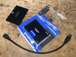Dwa dyski SSD, adapter USB na SATA i kabel USB na drewnianym tle.