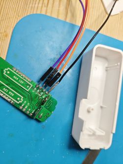 Green printed circuit board with attached wires on a blue pad, next to a white plastic casing.