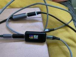 Kable USB C podłączone do miernika napięcia i prądu na żółtym tle.