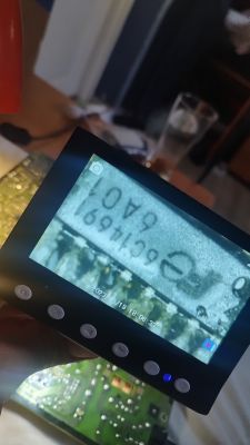 Osoba trzyma w ręku mikroskop cyfrowy, na ekranie wyświetlony jest powiększony obraz układu scalonego z oznaczeniem 9C1K961 8A01.