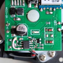Close-up of a green PCB with SMD parts, a 220 µF capacitor, and a visible soldered IC area