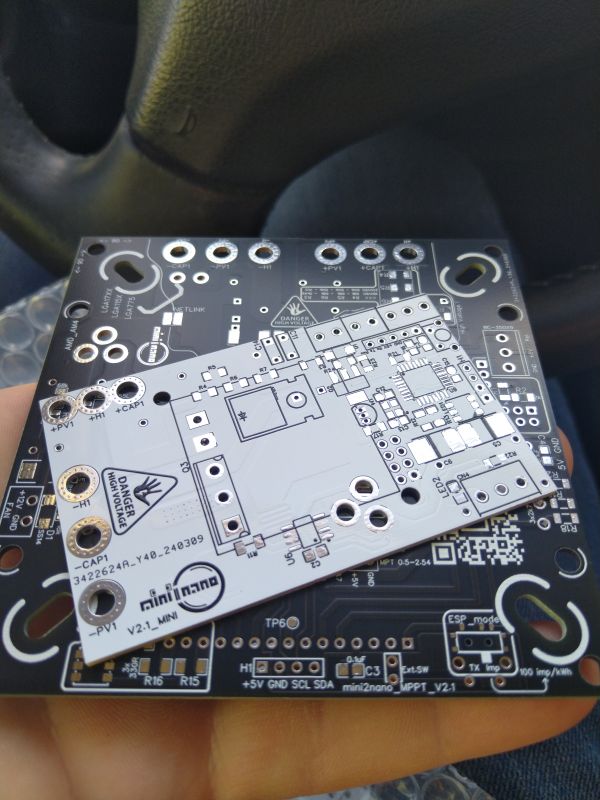 Two new PCBs stacked on top of each other on a hand with a car interior in the background. The boards feature markings and spots for electronic components.