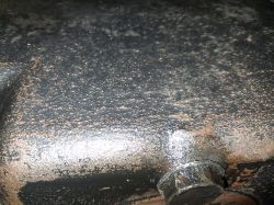 Zbliżenie na ciemną, chropowatą metalową powierzchnię z nalotem i śrubą przy dole kadru.