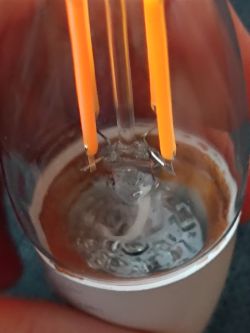 Close-up of a light bulb interior with two thin orange wires and a white wire at the bottom.
