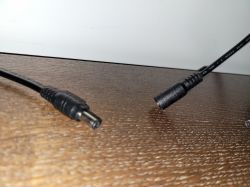 Power plug on the left and power strip socket on the right on a wooden surface.