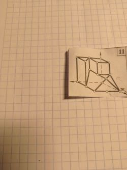 Zdjęcie części kartki z rysunkiem geometrycznym bryły na tle kratkowanego papieru.