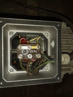 Zbliżenie na skrzynkę przyłączeniową silnika elektrycznego z przewodami i mostkami podłączeniowymi.