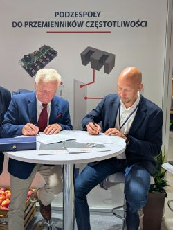 Dwóch mężczyzn podpisuje dokumenty przy okrągłym stole na tle baneru DACPOL