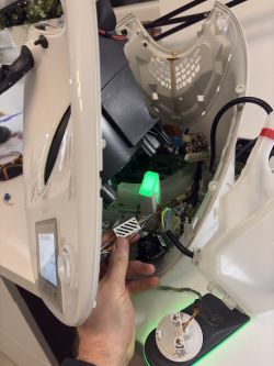 Otwarty biały robot kuchenny, dłoń trzyma przewody i płytkę; wewnątrz świeci zielona dioda