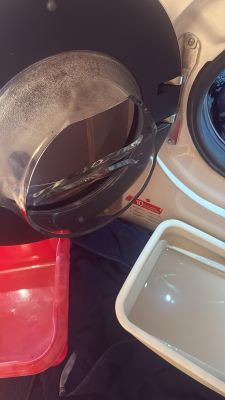 Pęknięte szkło drzwiczek pralki Hoover, widoczne z bliska z miskami pod spodem.
