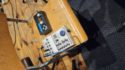 Na drewnianym krześle leżą dwa urządzenia elektroniczne audio z pokrętłami i przewodami.