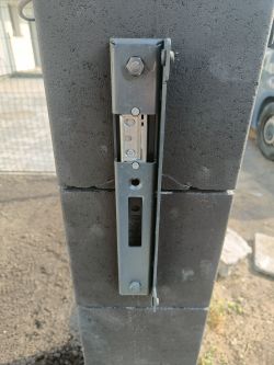 Zbliżenie na zamontowany mechanizm zamka mechanicznego w furtce na murku z szarego betonu.