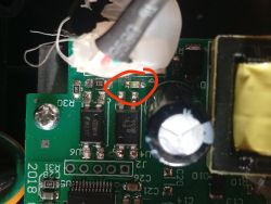 Zbliżenie płytki PCB z zaznaczonym czerwonym kółkiem elementem SMD obok kondensatora i transformatora