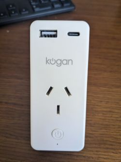 Kogan Smart Plug with USB Ports Kogan smart plug with USB ports lying on a wooden surface.