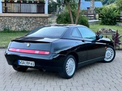 Black Alfa Romeo sports car parked on a paved driveway.