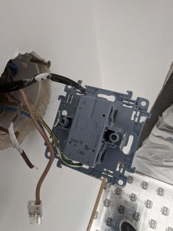 Podwójny włącznik światła Simon 10 zamontowany w ścianie z widocznymi przewodami elektrycznymi.