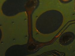 Zbliżenie na płytkę drukowaną z widocznymi ścieżkami i otworami.