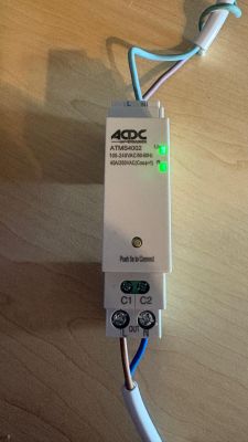White ACDC ATMS4002 module with two green LEDs, connected wires on a wooden surface.