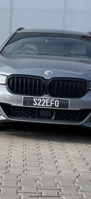 Przód szarego samochodu marki BMW z rejestracją S22EFO, stojącego na brukowanym podjeździe.