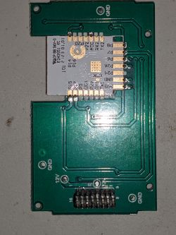 View of an electronic module mounted on a green circuit board with pin markings.