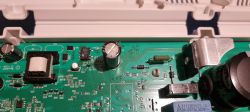 Zbliżenie na płytkę drukowaną z widocznymi kondensatorami i innymi komponentami elektronicznymi.