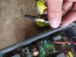 Close-up of a burnt electronic component held above an open electronic device.